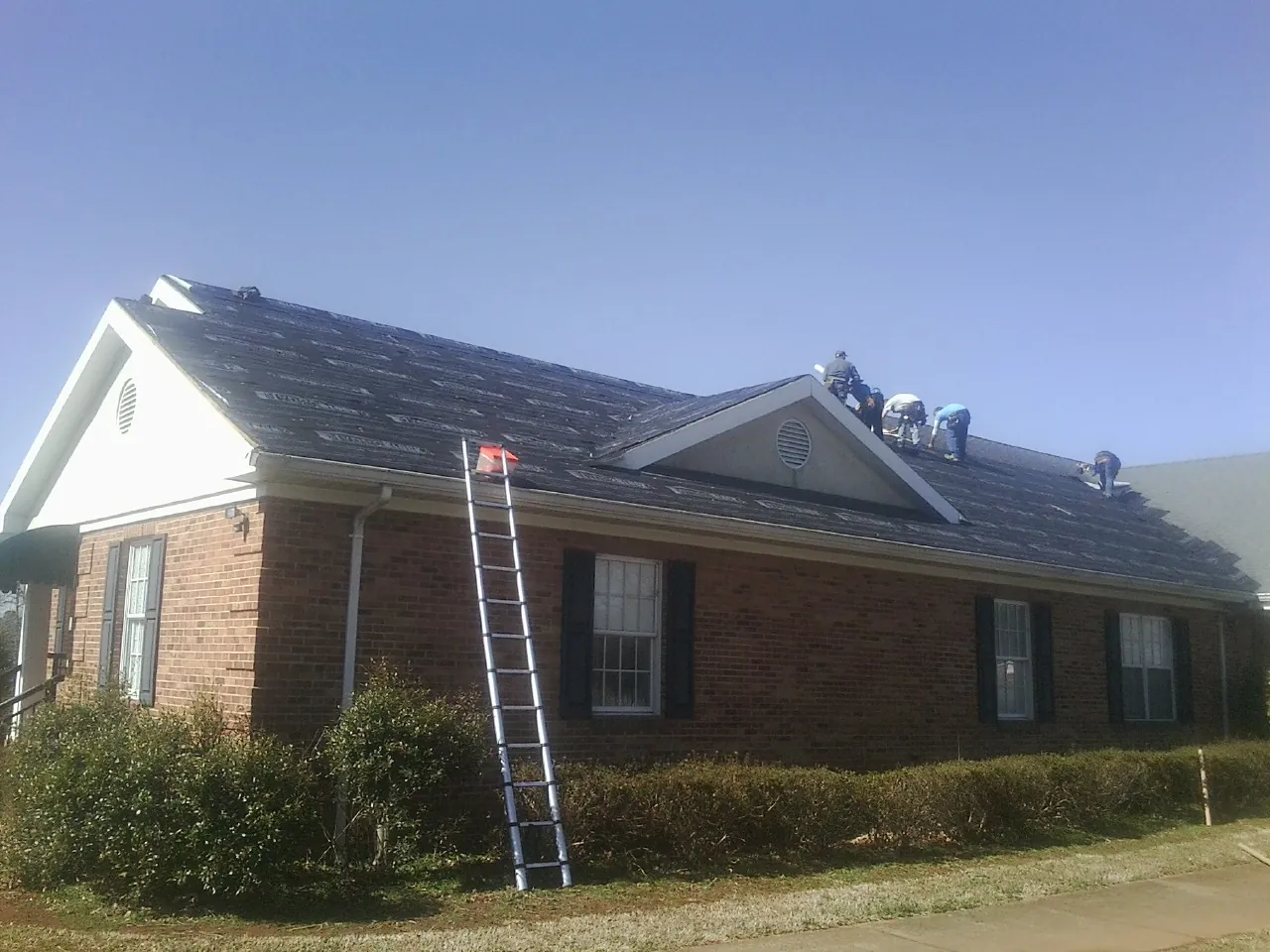 Crew tearing shingles off a brick ranch roof with a ladder set — Emergency Roof Repair work by our crew in Lake Oswego