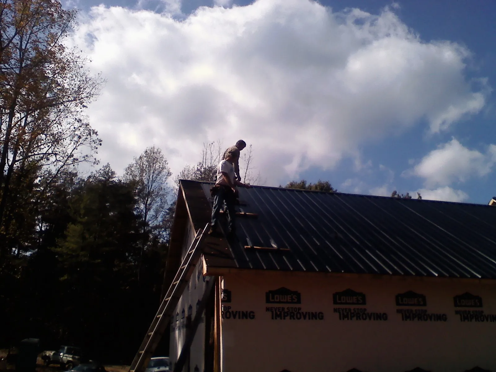 Roofer fastening dark metal panels high against a cloudy sky, from a Roof Inspection job in Lake Oswego
