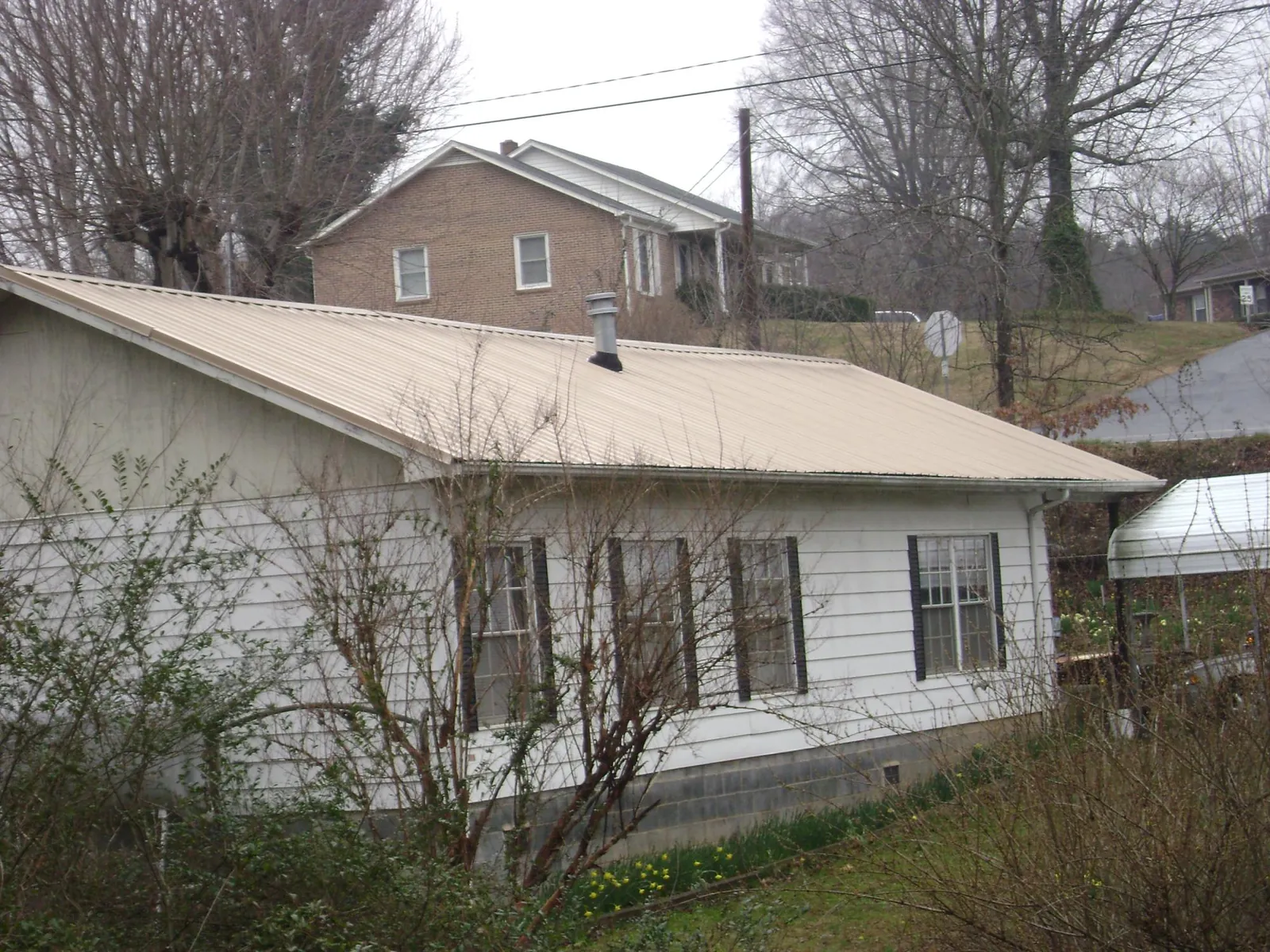 Tan metal roof on a white sided house set into a hillside — Commercial Roofing by Roofing Brothers in Lake Oswego
